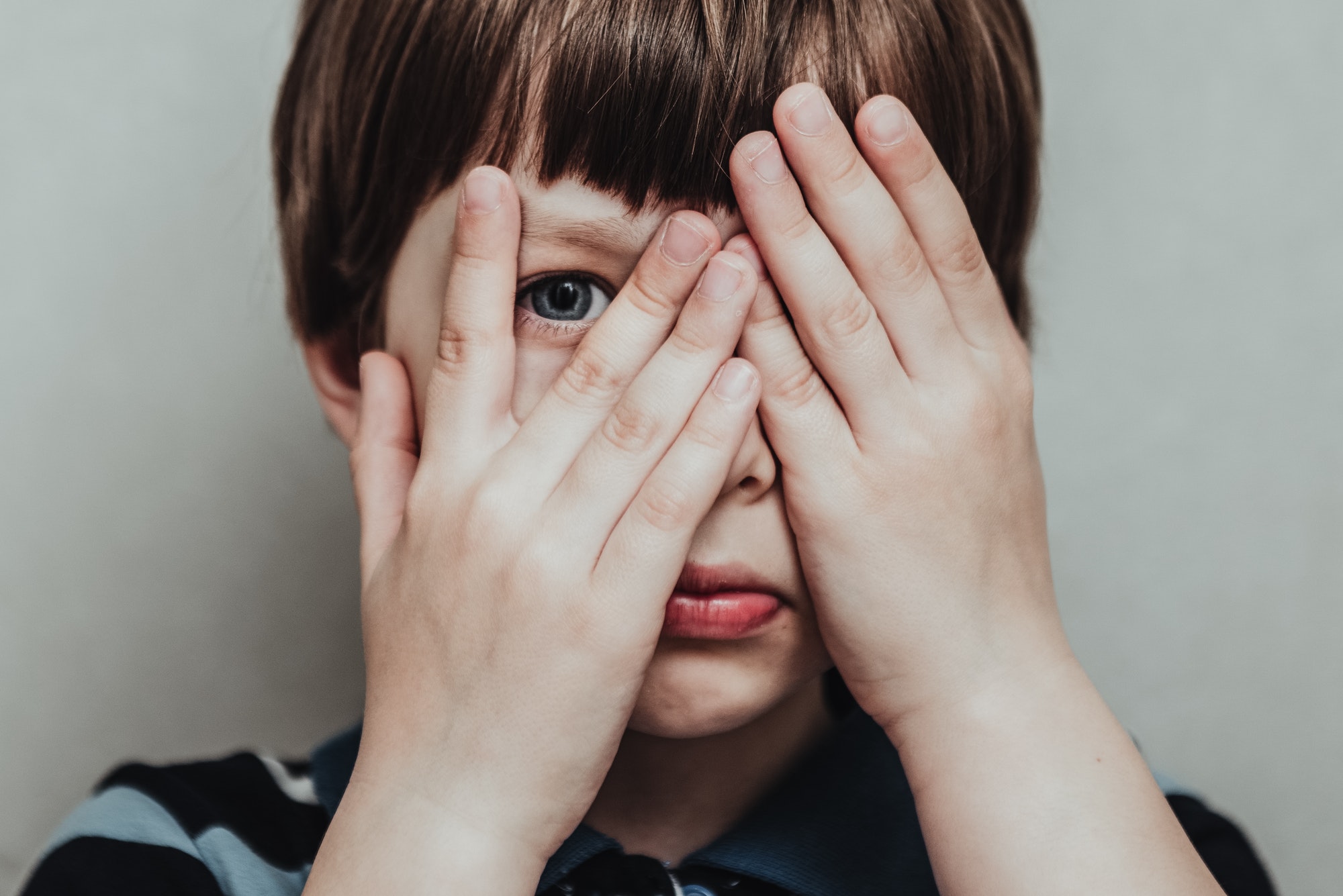 Unhappy kid boy hands hides his face, child mental health concept, world autism awareness day